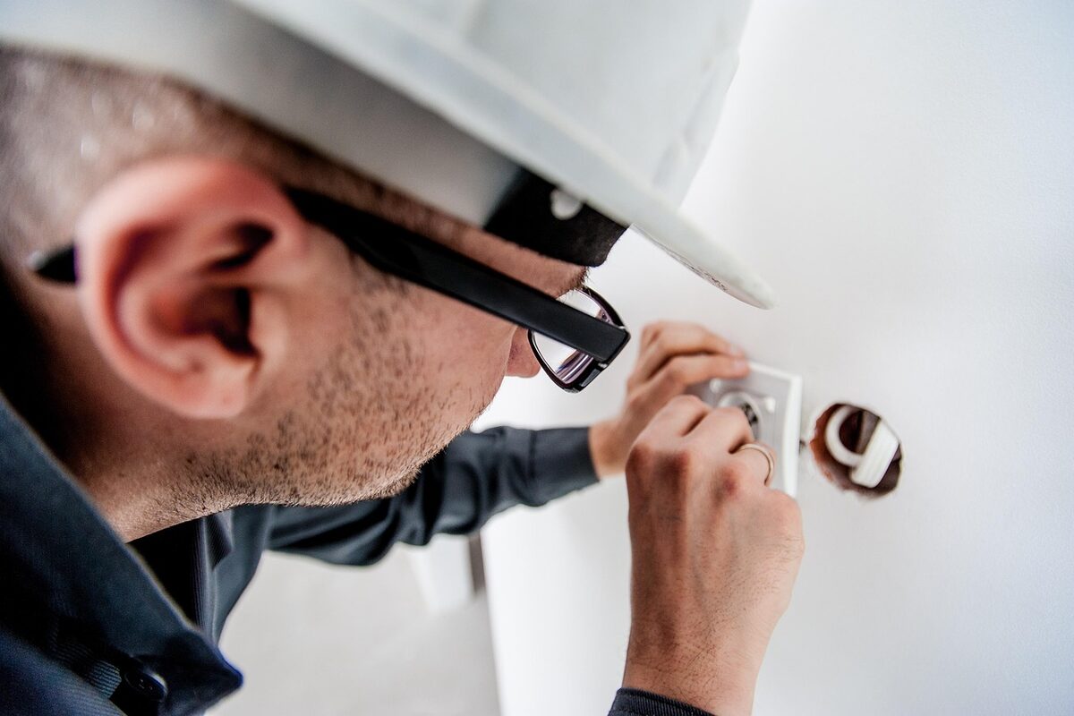 Qualified South African electrician with safety glasses and hard hat inspecting a residential electrical fitting during a Certificate of Compliance assessment