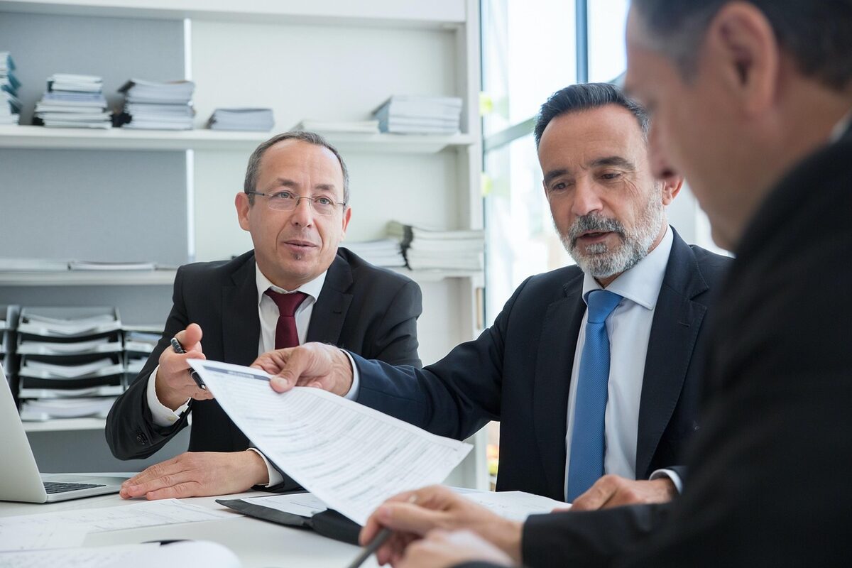 Three professional advisors in a modern office reviewing an electrical Certificate of Compliance document together